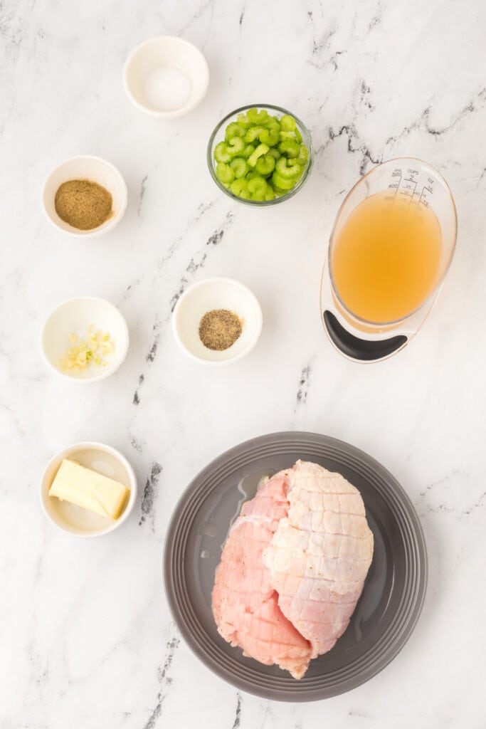 Overhead view of ingredients for Instant Pot Turkey Breast including butter, spices, garlic, celery, broth, and a raw turkey breast on a plate.