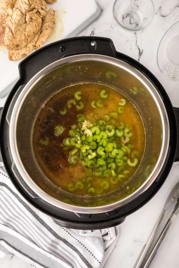Instant Pot filled with broth, garlic, and celery to create flavorful liquid for pressure cooking turkey.