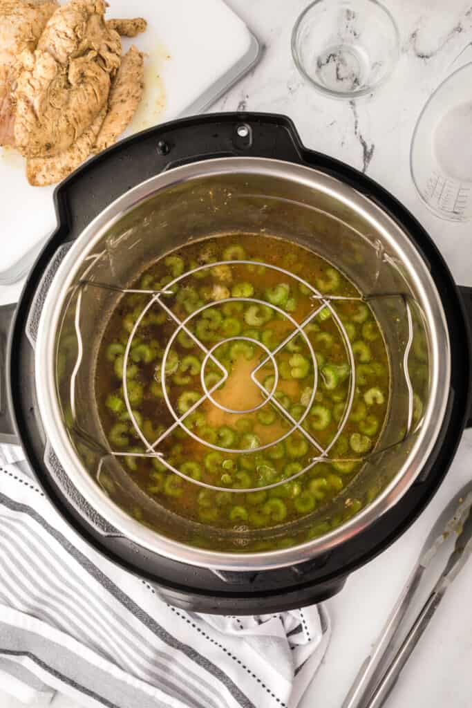 Instant Pot with celery and broth inside, showing the metal trivet in place before adding the turkey.