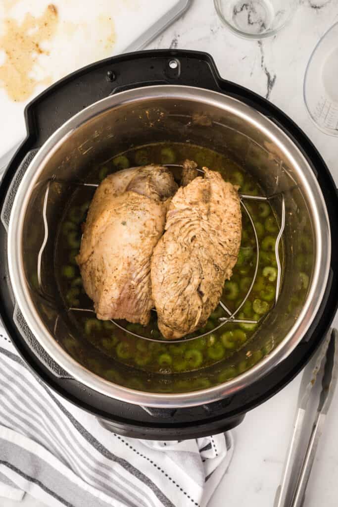Seared turkey breast resting on trivet inside the Instant Pot over broth and celery, ready to cook under pressure.