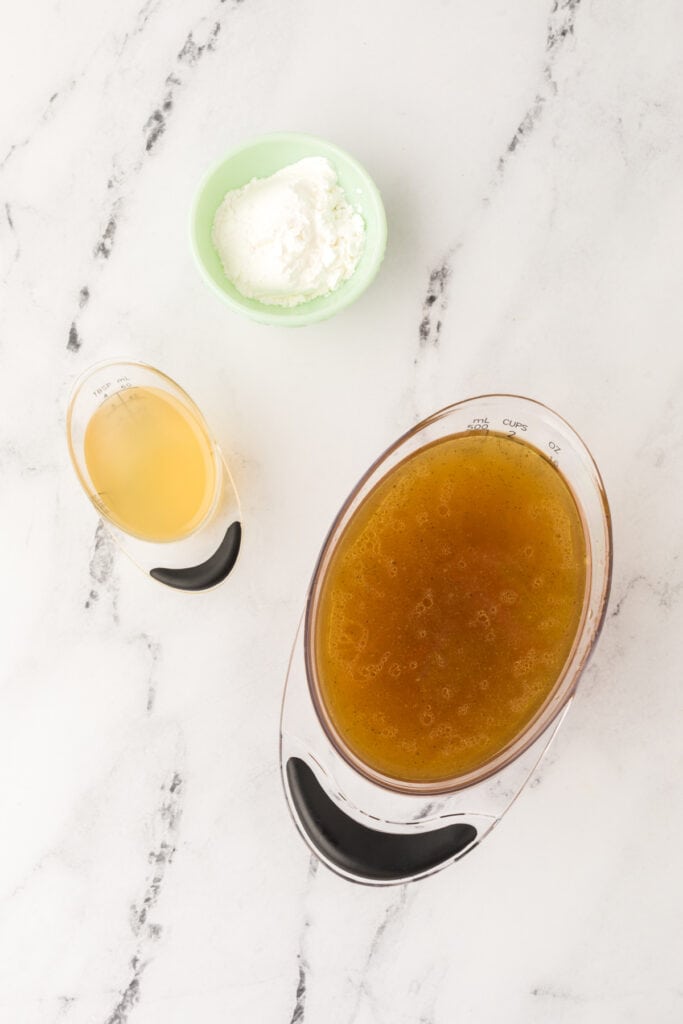 Overhead view of cornstarch, broth, and strained turkey drippings arranged for making gravy.