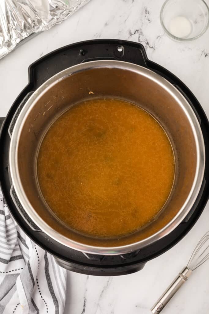 Instant Pot filled with simmering brown gravy after thickening, whisk placed nearby on the counter.