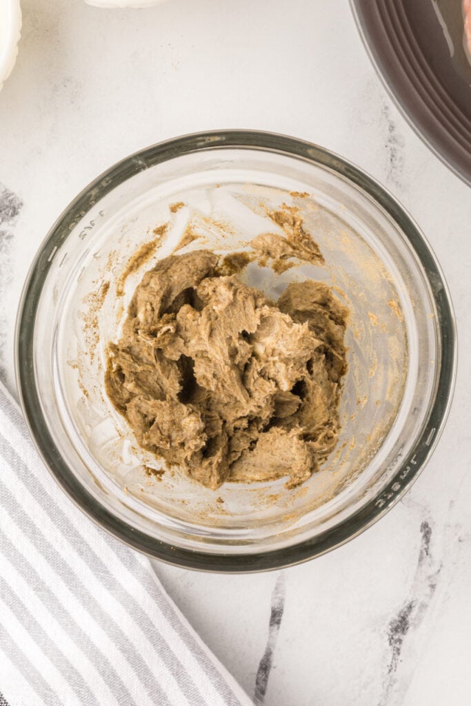 Mixed butter and seasoning forming a smooth herb butter in a glass bowl for turkey coating.