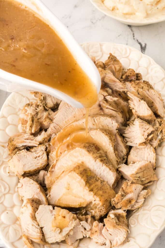 Gravy being poured over sliced turkey breast on a white serving platter for a cozy dinner presentation.