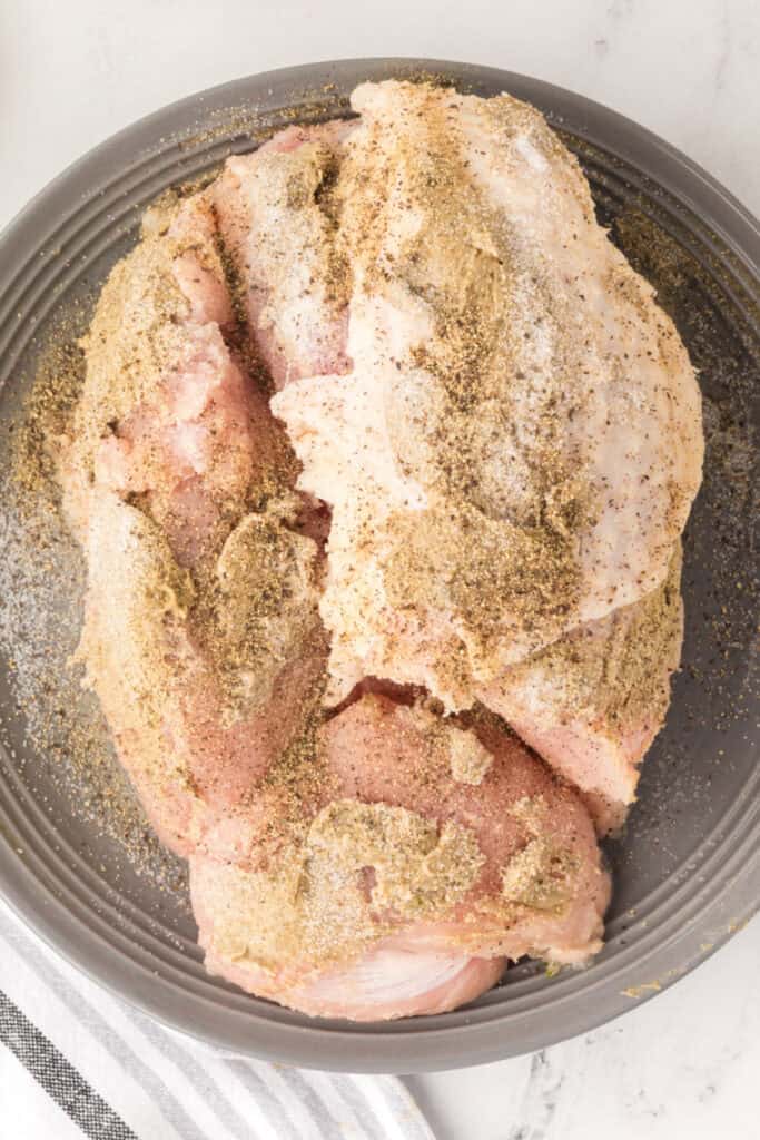 Seasoned turkey breast sprinkled with salt and pepper on a gray plate before searing.