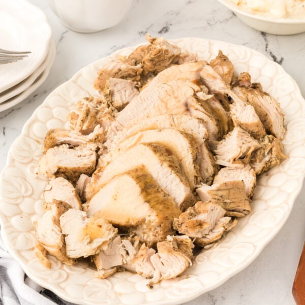 Square image of sliced Instant Pot turkey breast on a white platter with gravy on top, styled for social media or featured use.