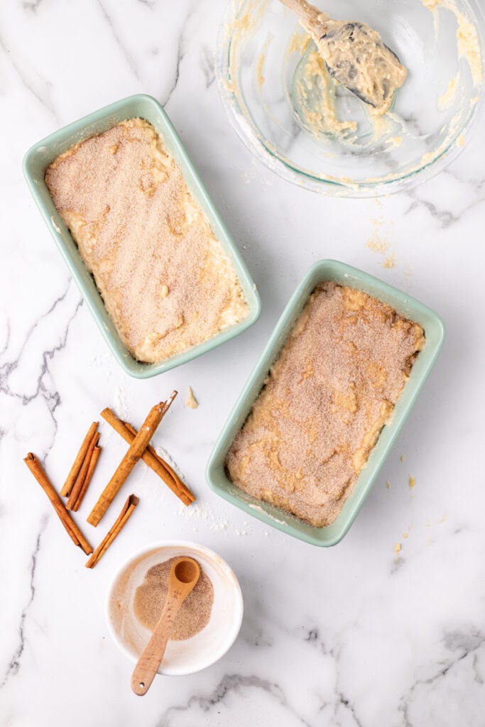 cinnamon-sugar topping sprinkled over the final layer of batter in both loaf pans, ready to swirl and bake