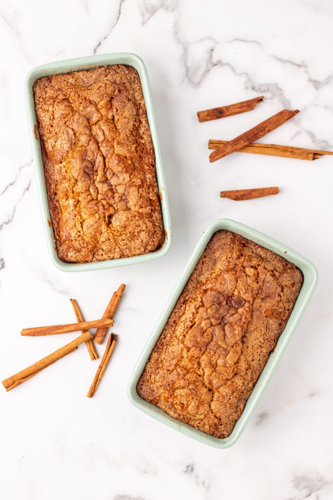 two freshly baked Amish Cinnamon Bread loaves with a golden cinnamon-sugar crust still in the green loaf pans