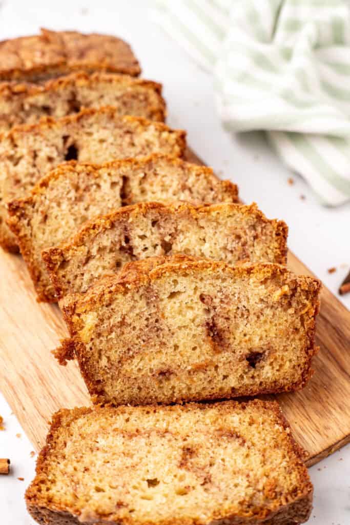 slices of Amish Cinnamon Bread fanned out on a wooden cutting board showing the soft crumb and cinnamon swirl