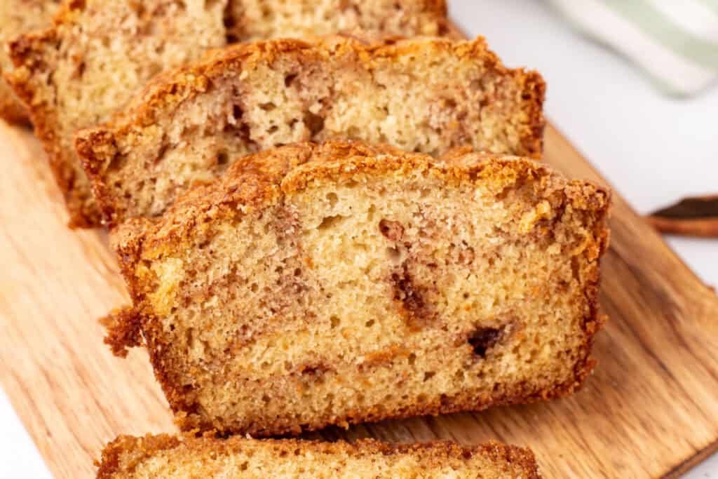 angled close-up of a thick slice of Amish Cinnamon Bread on a cutting board showing the tender crumb and cinnamon swirl throughout