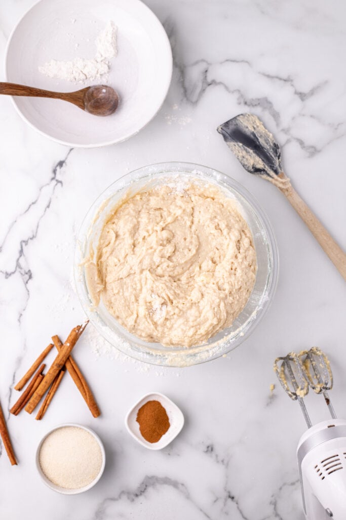 completed Amish Cinnamon Bread batter in a glass bowl with a rubber spatula and handheld mixer nearby