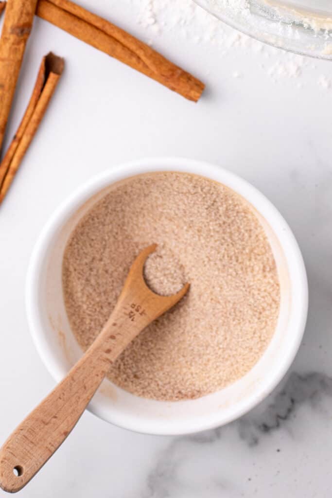 cinnamon-sugar topping mixed together in a small white bowl with a wooden measuring spoon