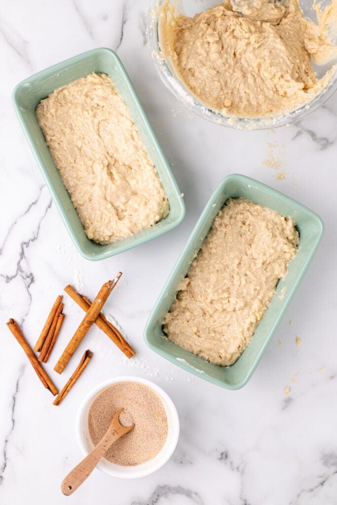 first layer of Amish Cinnamon Bread batter divided between two green loaf pans on a marble surface