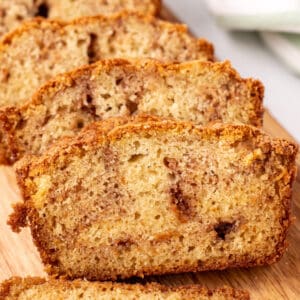 close-up square image of sliced Amish Cinnamon Bread stacked on a cutting board showing the golden crust and soft cinnamon-swirled crumb