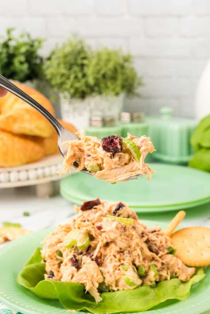 fork holding a bite of chicken salad with Miracle Whip above a plate with lettuce and crackers
