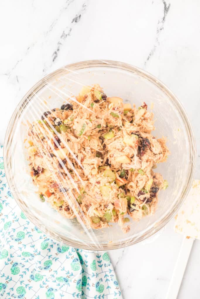 chicken salad with Miracle Whip covered with plastic wrap in a glass bowl for chilling