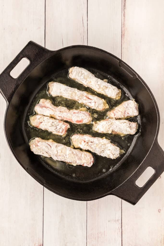 Heat 2 tablespoons of the oil in a skillet over medium heat. Add half of the strips and brown on both sides. 