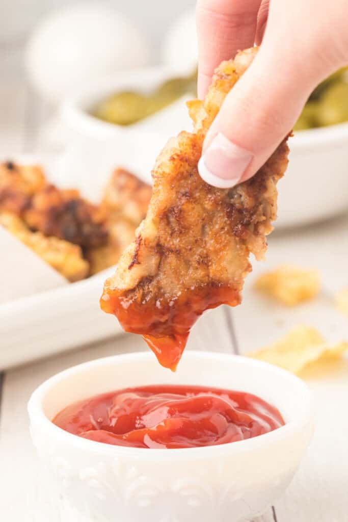 hand dipping a steak finger into ketchup