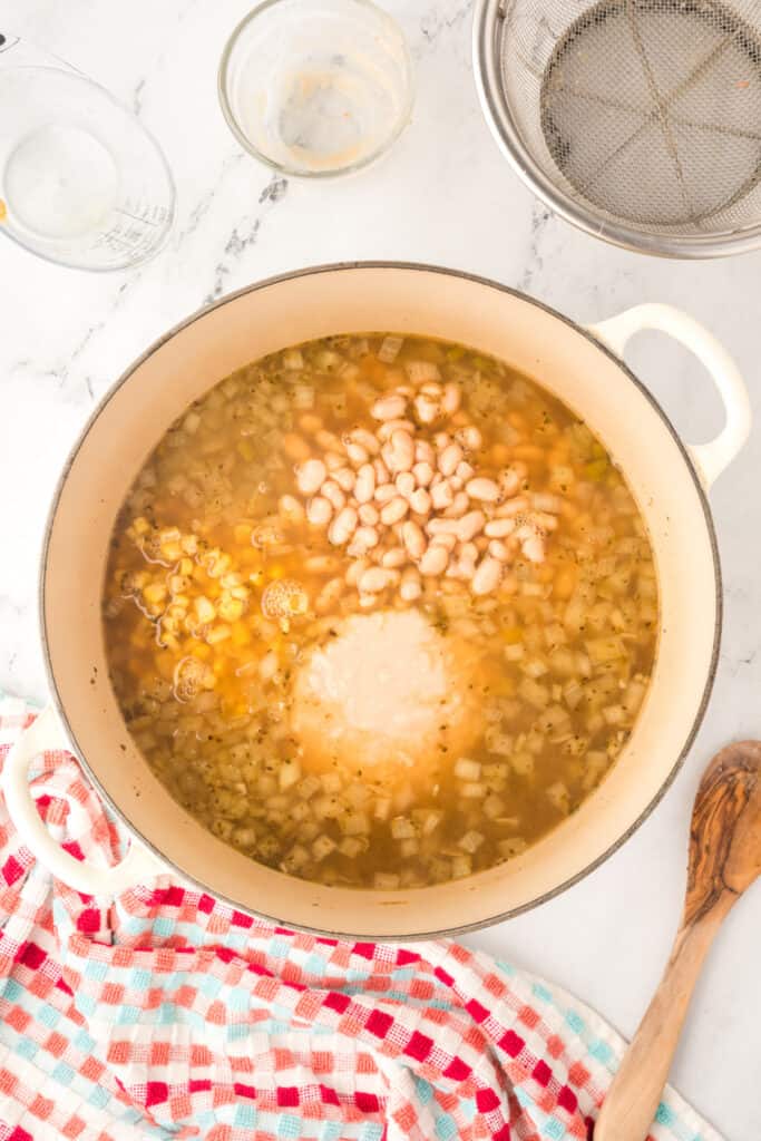 Dutch oven filled with simmering broth, corn, whole beans, and pureed beans combined.
