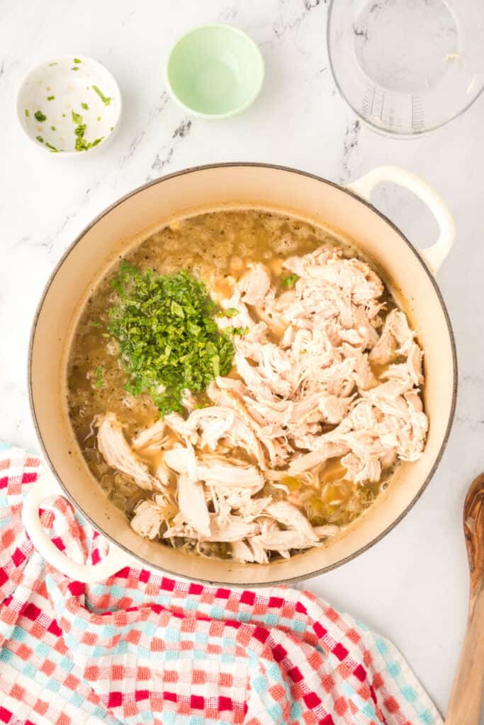 Shredded chicken and fresh cilantro added to the pot of chili before stirring.