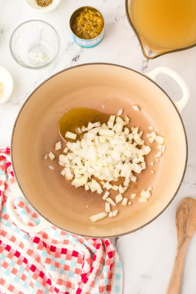 Chopped onions added to olive oil in a large cream-colored dutch oven, ready to sauté.