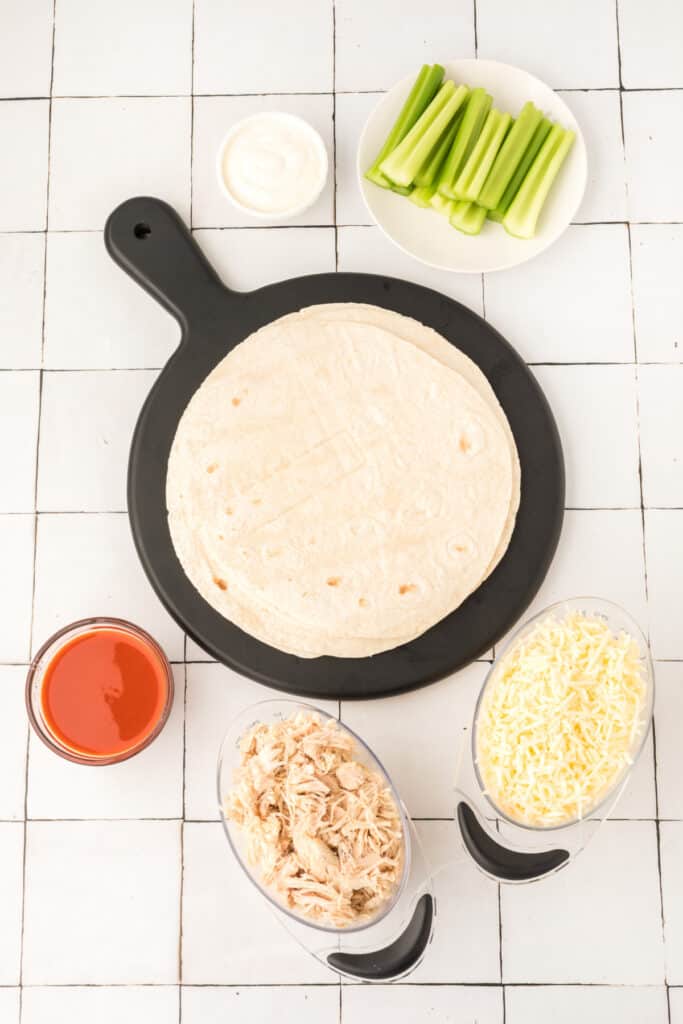 Ingredients for Buffalo Chicken Quesadillas including tortillas, shredded chicken, buffalo sauce, Monterey Jack cheese, celery, and ranch dressing