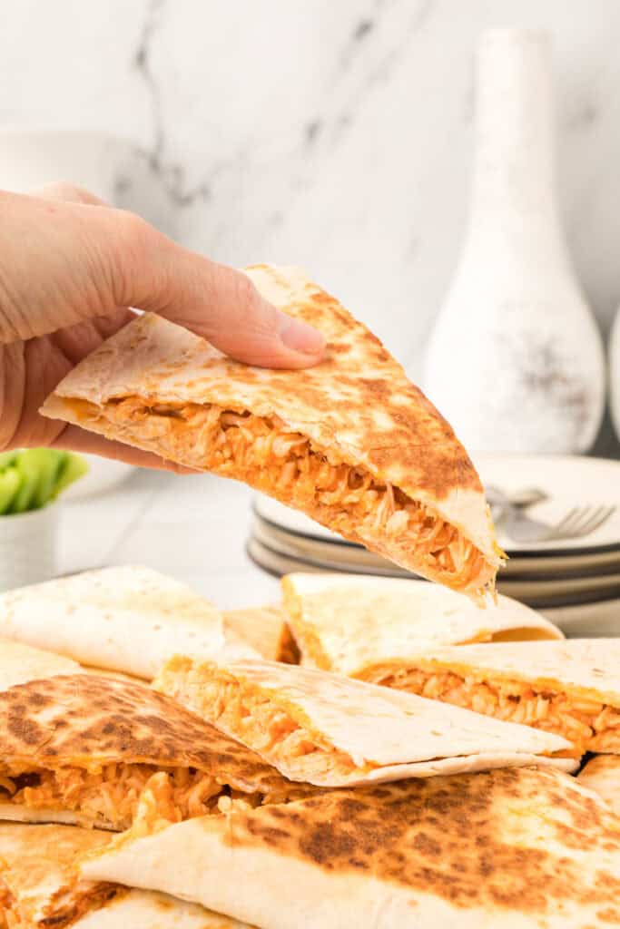 Hand holding a crispy Buffalo Chicken Quesadilla with shredded chicken filling