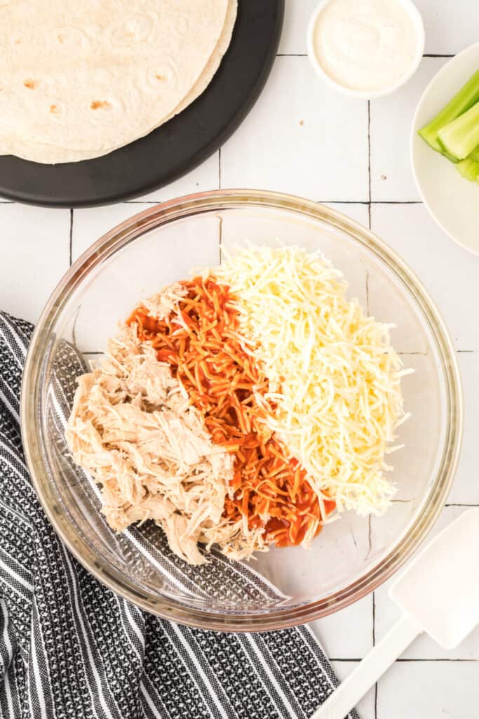 Shredded chicken, buffalo sauce, and Monterey Jack cheese in a bowl for Buffalo Chicken Quesadillas