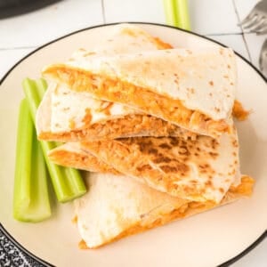 Buffalo Chicken Quesadillas stacked on a plate with celery sticks and cheesy buffalo chicken filling visible