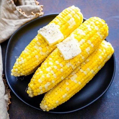 cooked corn on the cob with butter on black plate