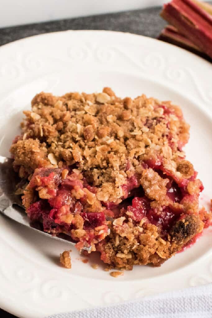 Angled view of a slice of rhubarb crisp on a plate, with crisp topping and red rhubarb filling.