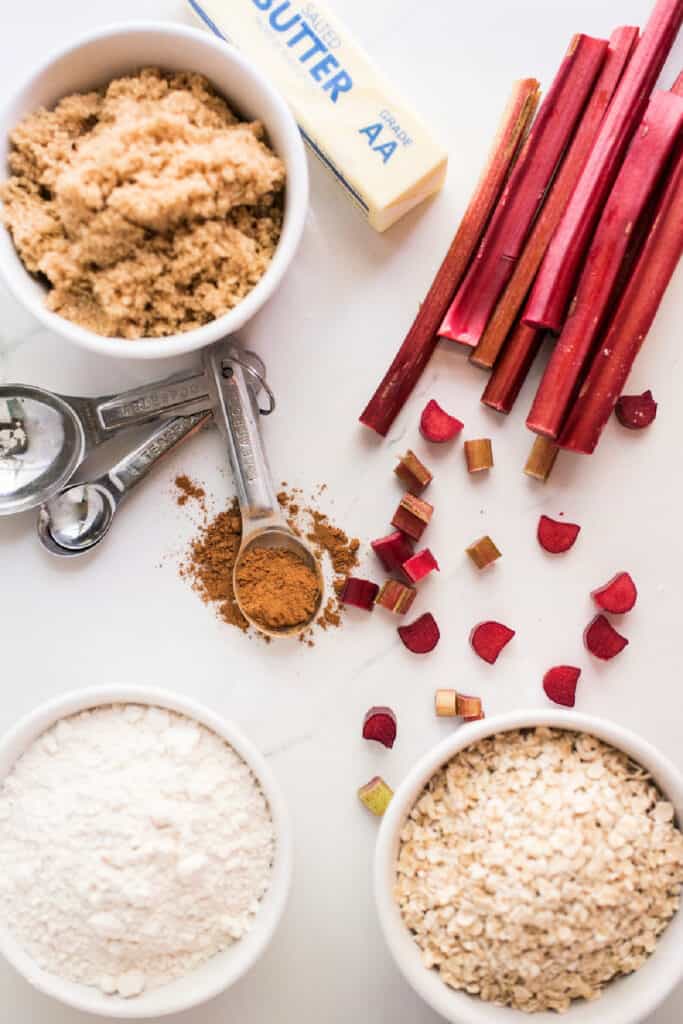 Overhead shot of ingredients for rhubarb crisp including flour, oats, brown sugar, cinnamon, butter, and chopped rhubarb.