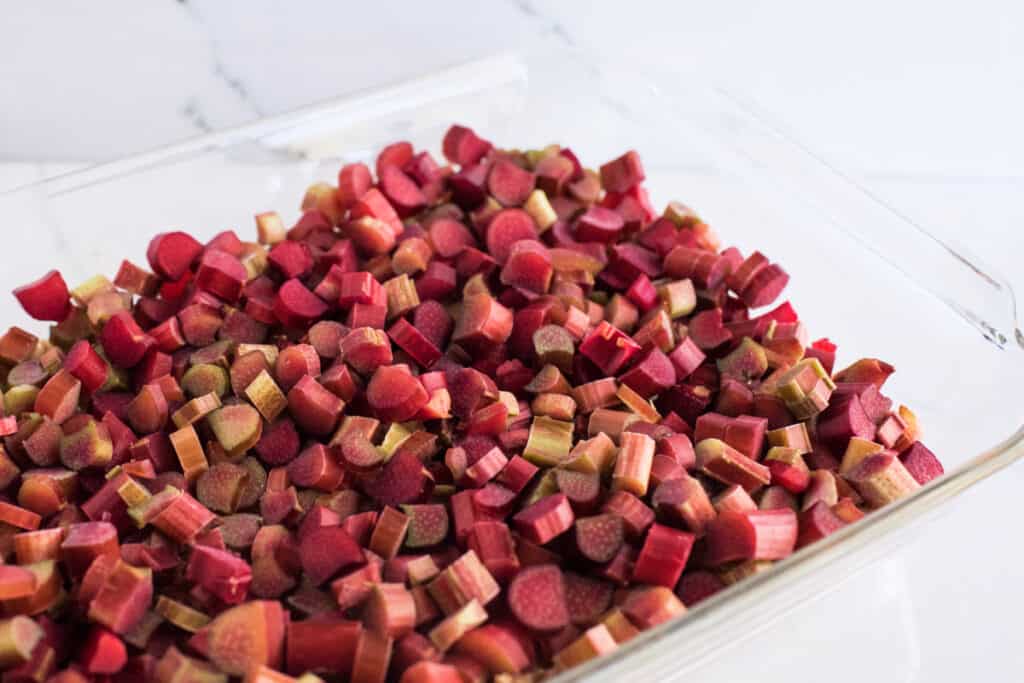 Chopped rhubarb spread out in a clear glass baking dish, ready to be used in the crisp.