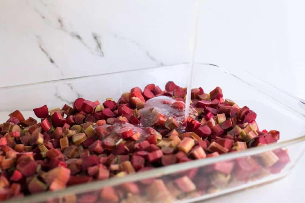 Sugar sauce being poured over chopped rhubarb in a baking dish for rhubarb crisp.