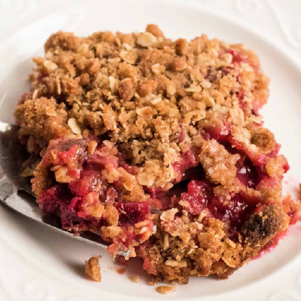 Square crop of a rhubarb crisp serving with oat topping and juicy filling on a white plate.
