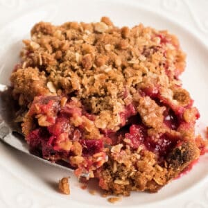 Square crop of a rhubarb crisp serving with oat topping and juicy filling on a white plate.