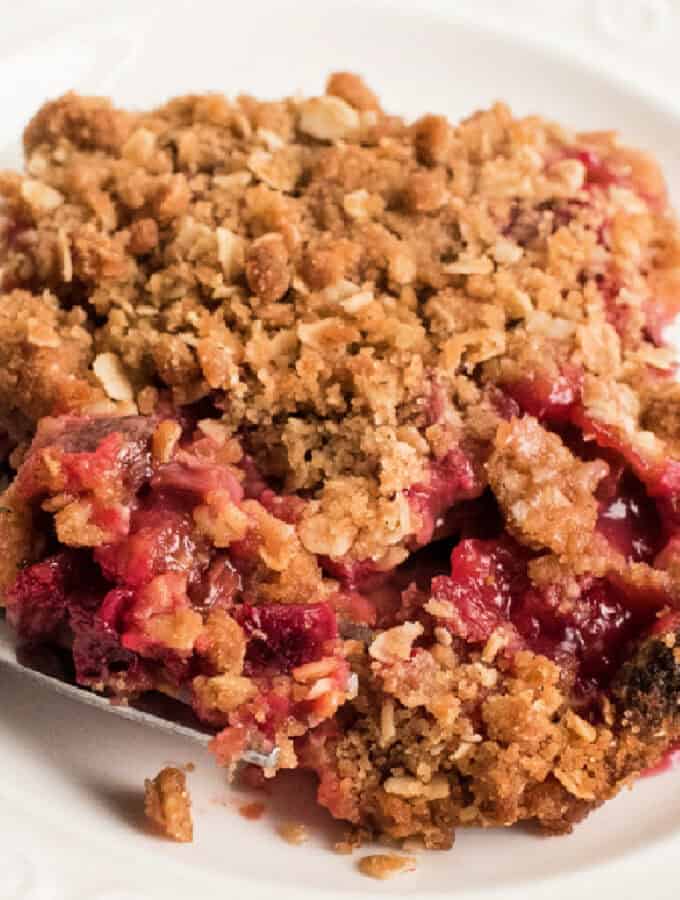 Square crop of a rhubarb crisp serving with oat topping and juicy filling on a white plate.