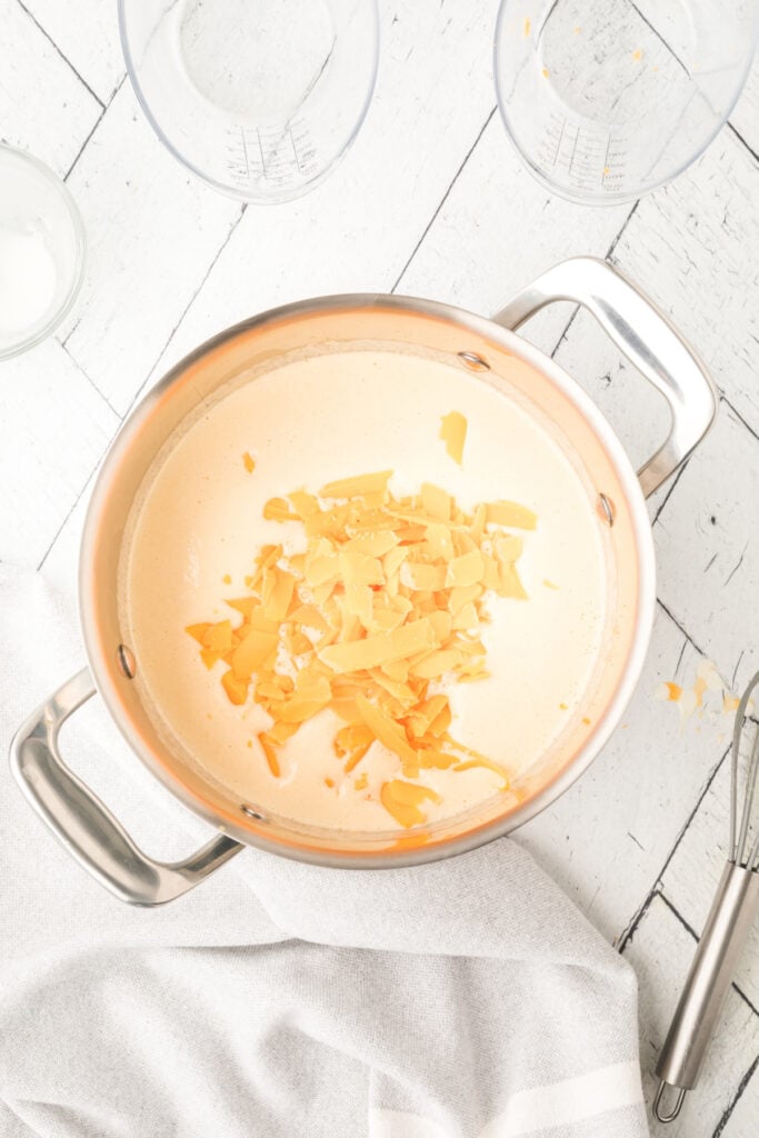 saucepan with shredded cheese added into the warm liquid mixture