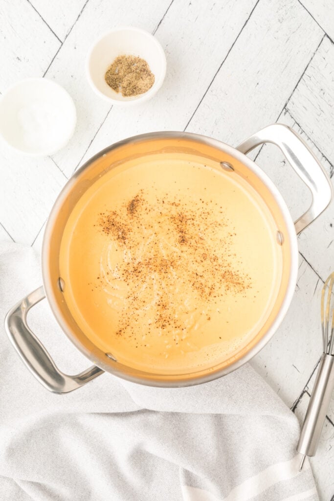saucepan with black pepper sprinkled over creamy cheese sauce