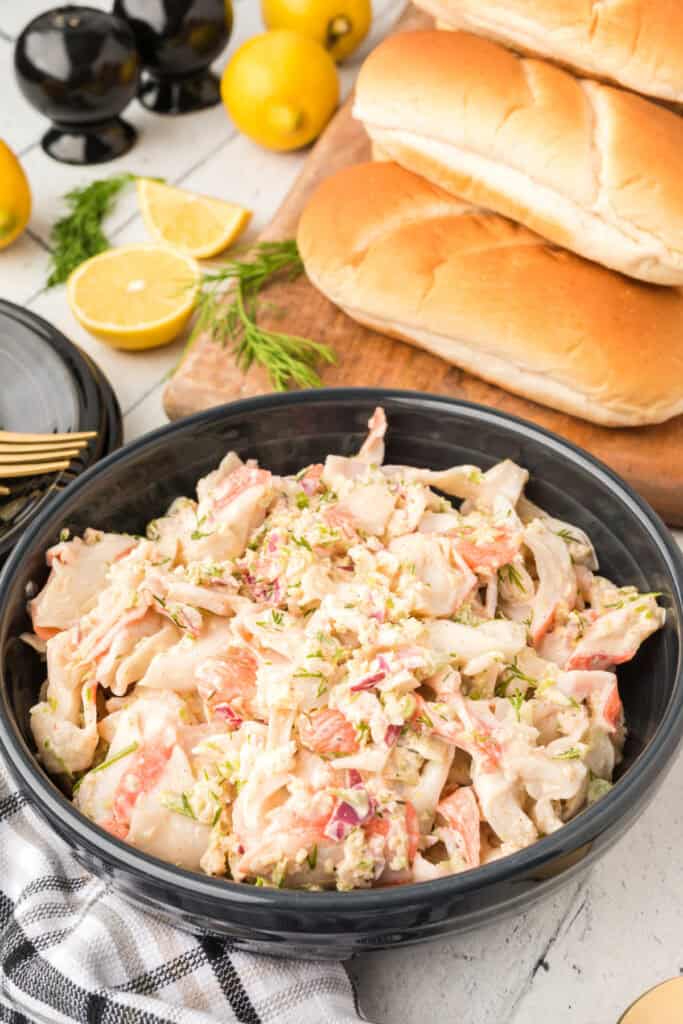Creamy homemade crab salad served in a black bowl with sandwich rolls and fresh lemon wedges.