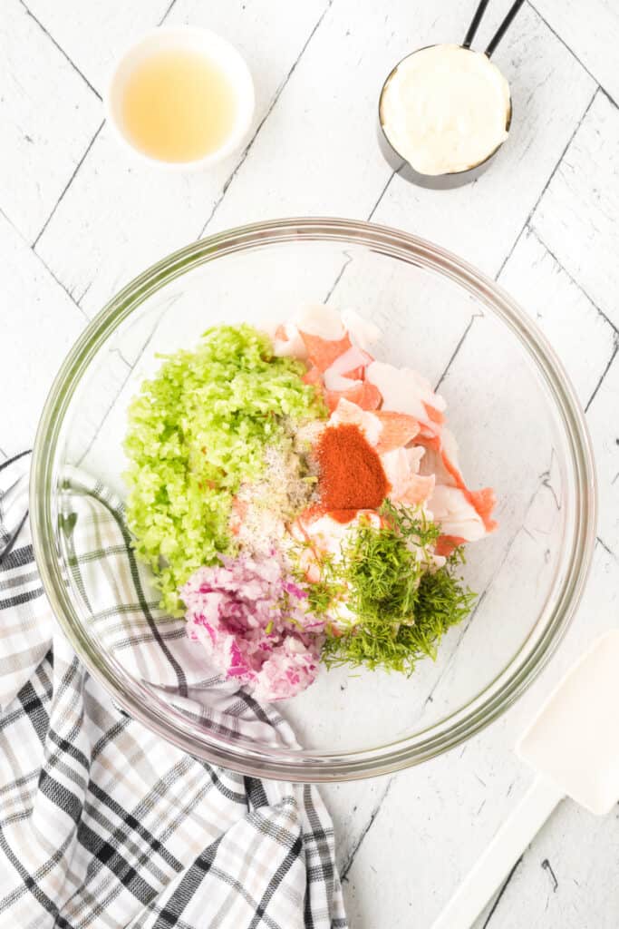 Imitation crab, celery, red onion, fresh dill, mayonnaise, lemon juice, and seasonings combined in a glass mixing bowl for Deli-Style Crab Salad.