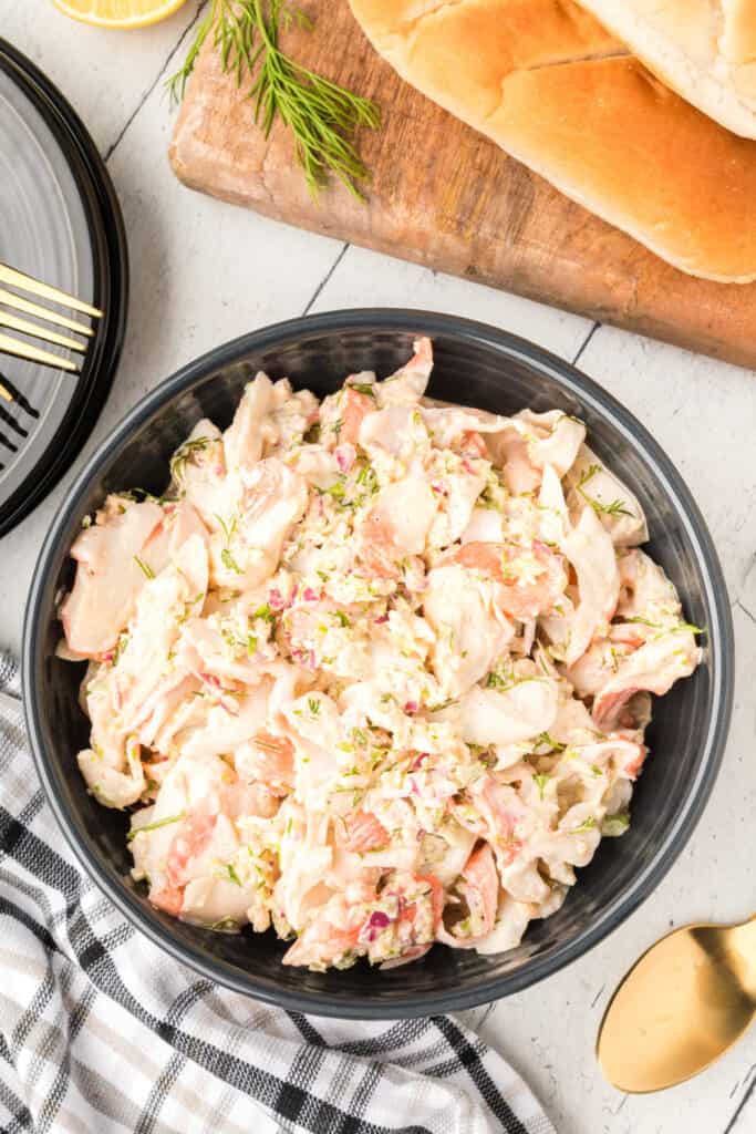 Creamy homemade crab salad served in a black bowl with sandwich rolls and fresh lemon wedges.