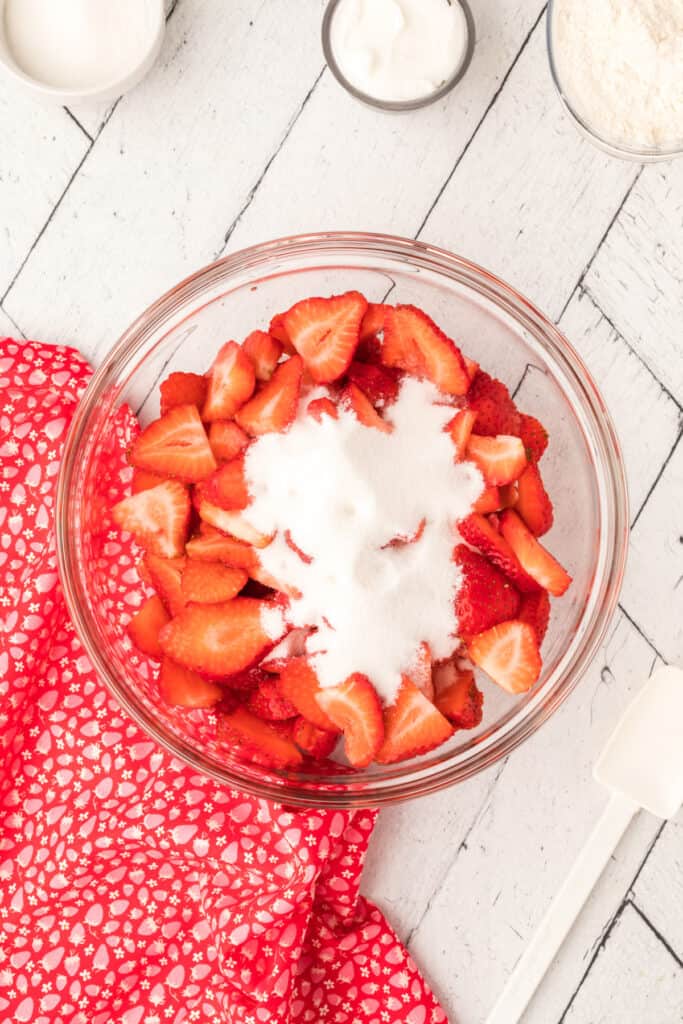 Sliced strawberries in a glass bowl with sugar sprinkled on top.