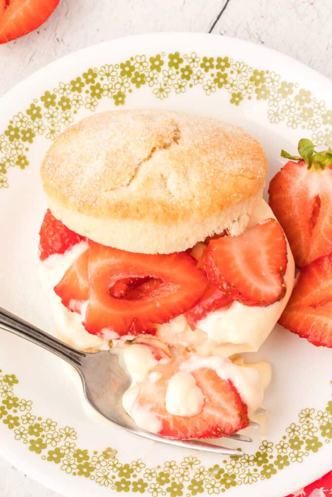 Partially eaten shortcake with cream and strawberries, served on a plate with a fork.
