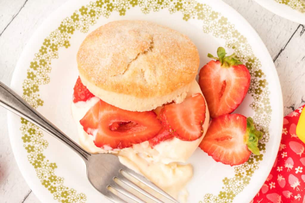 A plate with strawberry shortcake, sliced strawberries, and a fork.