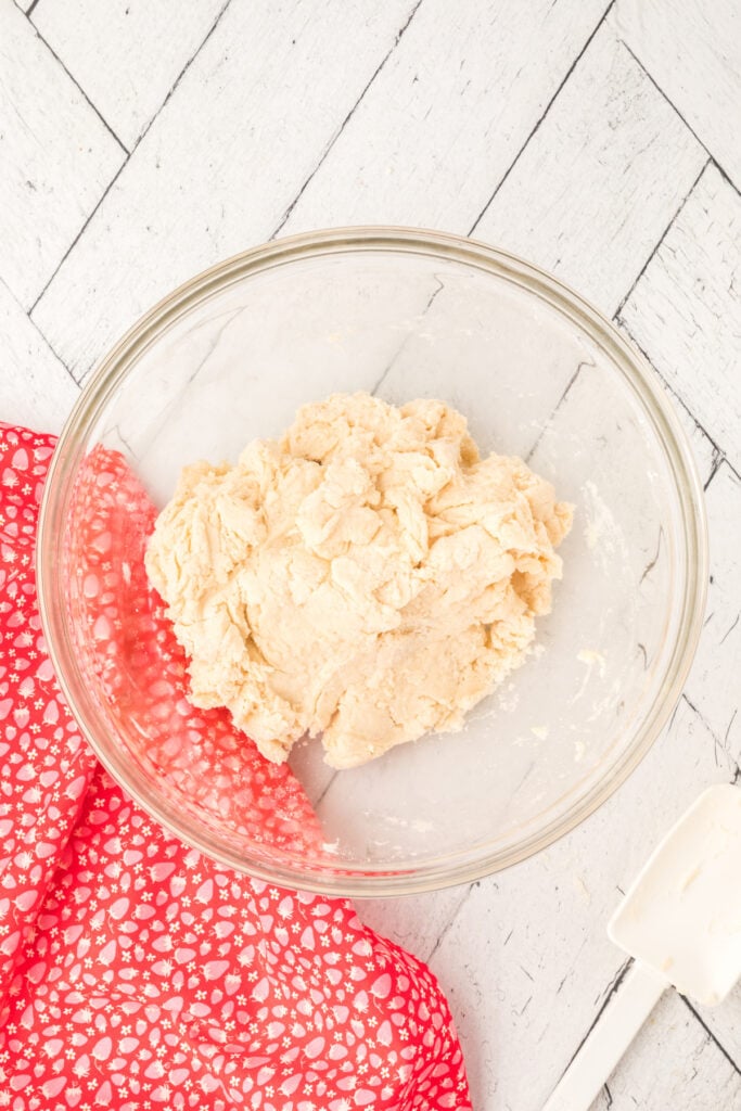 A bowl of biscuit dough next to a red patterned cloth and spatula.