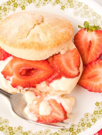 Strawberry shortcake on a plate with sliced strawberries and a fork.