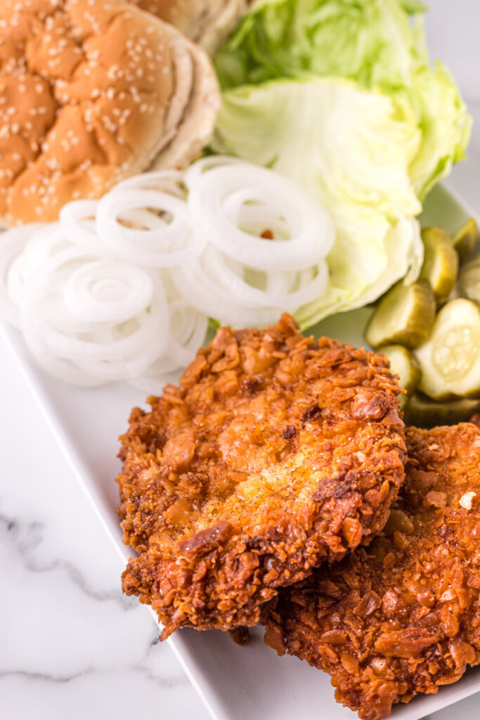cooked breaded pork tenderloins on serving platter with onions lettuce pickles and buns