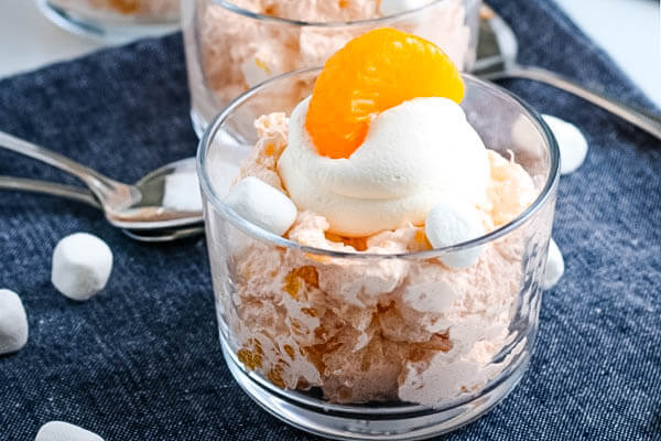 Mandarin Orange Fluff Salad in small glass bowl garnished with whipped topping and mandarin orange