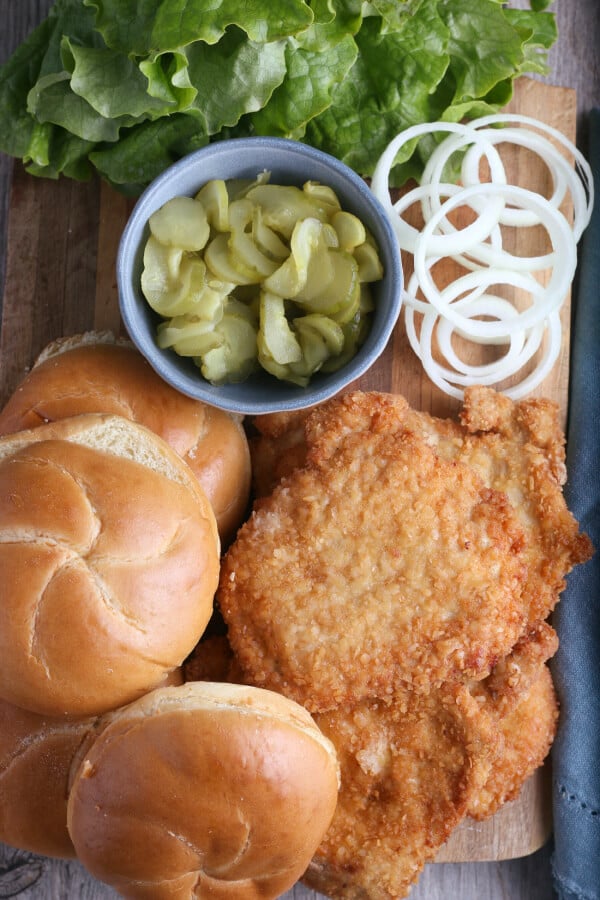 finished ingredients laid out on a cutting board to make breaded pork tenderloin sandwich